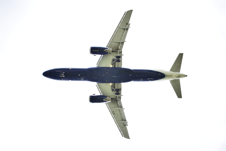 A JetBlue Airbus A320 photographed from below as it approaches LaGuardia Airport in New York on short final. The aircraft's sleek design and detailed undercarriage are highlighted against a bright, minimalist sky, showcasing the precision of modern aviation. - A Work By John Paglia