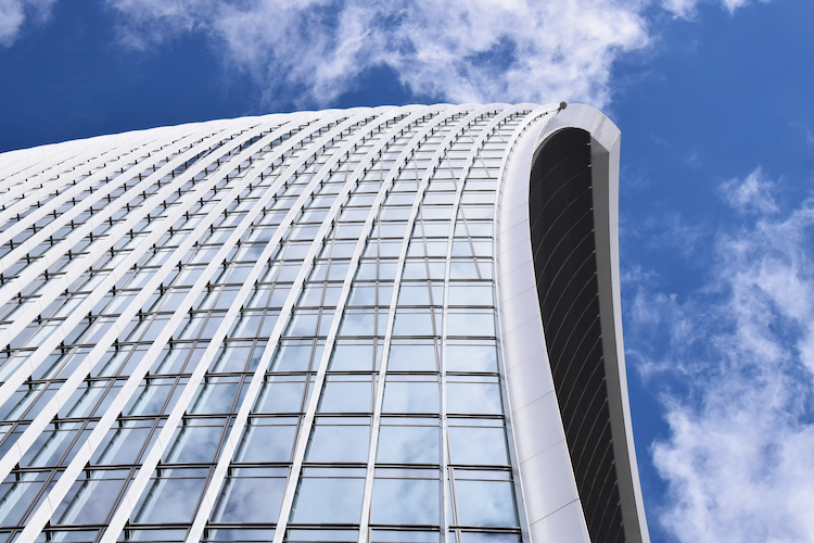 A photograph of 20 Fenchurch Street, also known as the “Walkie-Talkie” building, in London. The image highlights the building's distinctive curved facade with rows of reflective glass panels and sleek white metal framing. The architecture's unique design creates a striking contrast against the vibrant blue sky and scattered clouds above. Captured on a Nikon D5300 digital camera. A work by John Paglia.