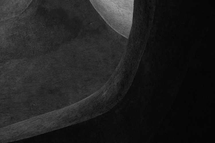 Abstract architectural detail of the interior of the new wing at New York's Natural History Museum. The black-and-white image emphasizes the smooth, curving forms of the structure, showcasing textured surfaces and interplay between light and shadow. The organic shapes evoke a sense of flow and timelessness, drawing attention to the modern design and intricate craftsmanship of the space. Captured on a Nikon D5300 digital camera. A work by John Paglia.