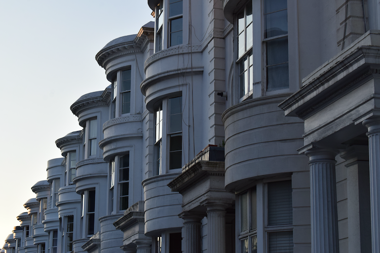 A row of elegant, white terraced houses in Paddington, London, showcasing classic architectural details such as rounded bay windows and decorative columns. The soft evening light enhances the timeless beauty of the façade, reflecting the charm of London's historic neighborhoods. Captured on a Nikon D5300 digital camera. A work by John Paglia.