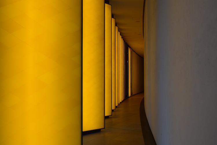 INSIDE THE HORIZON by Olafur Eliasson at the Fondation Louis Vuitton in Paris, France. This immersive installation features a sequence of glowing yellow panels set in a curved hallway, creating a dynamic interplay of light and geometry. The warm illumination of the panels contrasts with the adjacent neutral-toned wall, drawing attention to the gradual gradient of light as the artwork recedes into the distance. Eliasson's work explores themes of perception, light, and spatial awareness, inviting viewers to engage with their environment in a transformative way. Captured on a Nikon D5300 digital camera. A work by John Paglia.