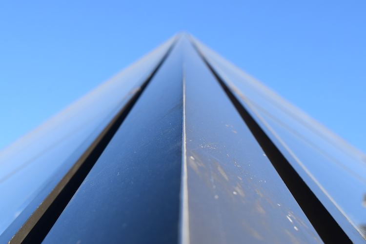 Close-up view of a corner section of the iconic glass pyramid designed by architect I. M. Pei at the Louvre Museum in Paris, France. The photograph captures the geometric precision and reflective surfaces of the pyramid against a clear blue sky. The angle emphasizes the sleek lines and modern architectural aesthetic, contrasting with the historic surroundings of the Louvre. The image highlights the seamless integration of contemporary design within a historic cultural landmark. Captured on a Nikon D5300 digital camera. A work by John Paglia.